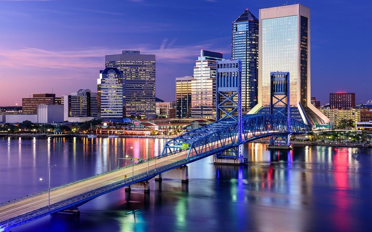 Downtown Jacksonville skyline at night, lit up over the St. Johns River and the blue Main Street Bridge